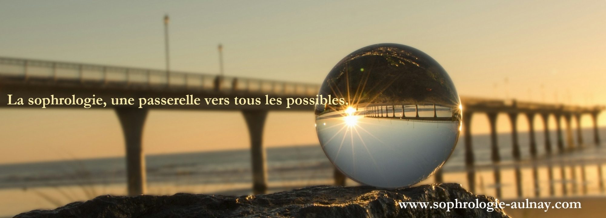 Une sphère de verre posée sur un rocher au bord de mer au coucher du soleil, devant une jetée. Le texte « La sophrologie, une passerelle vers tous les possibles » est incrusté sur l’image.
